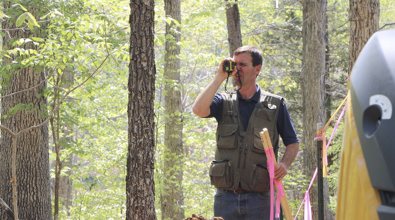 A Professional Soil Engineer From Soils Inc In The Middle Of A Forest Like Area Inspecting Something By The Magnifying Loupe