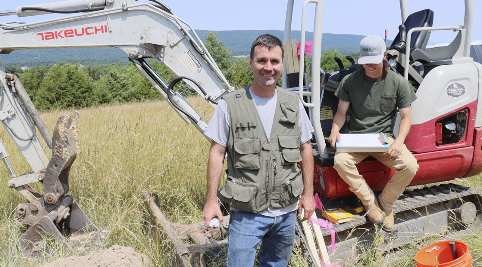 A Smiling Man From Soils Inc Facing The Camera Standing Ahead Of A Tractor During A Construction Inspection Of A House