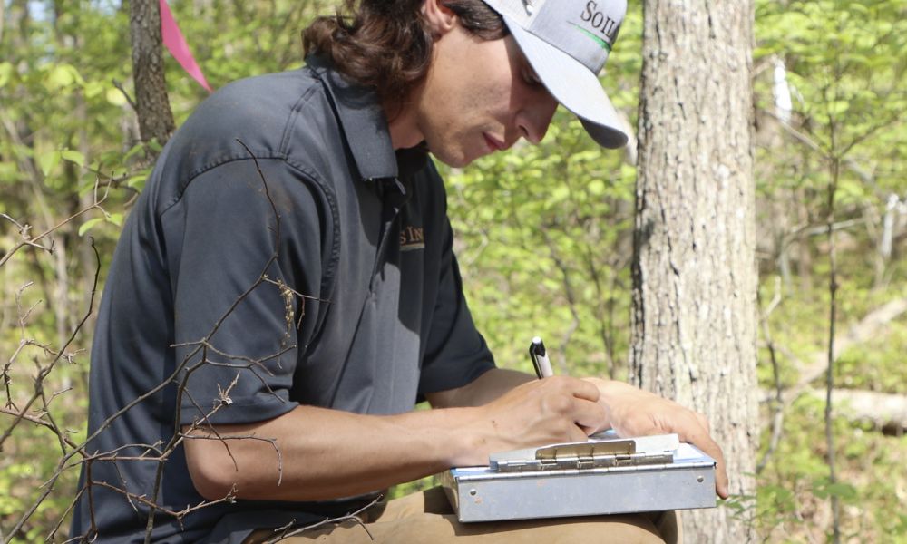 Closeup Shot Of A Professional Man From Soils Inc Sitting In A Forest Like Area With A Pen And Diary Noting Down Something