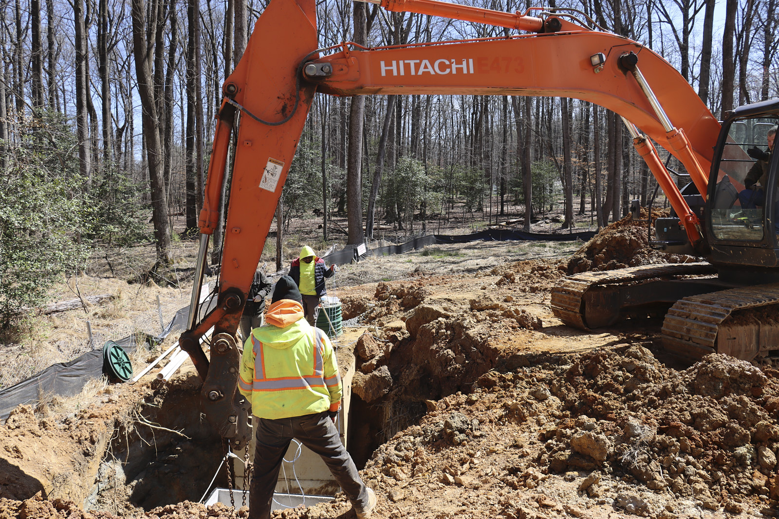 A Team Of Experts Using A Big Orange Tractor To Create A Large Dug Hole And Lowering Some Unknown Materials Into It