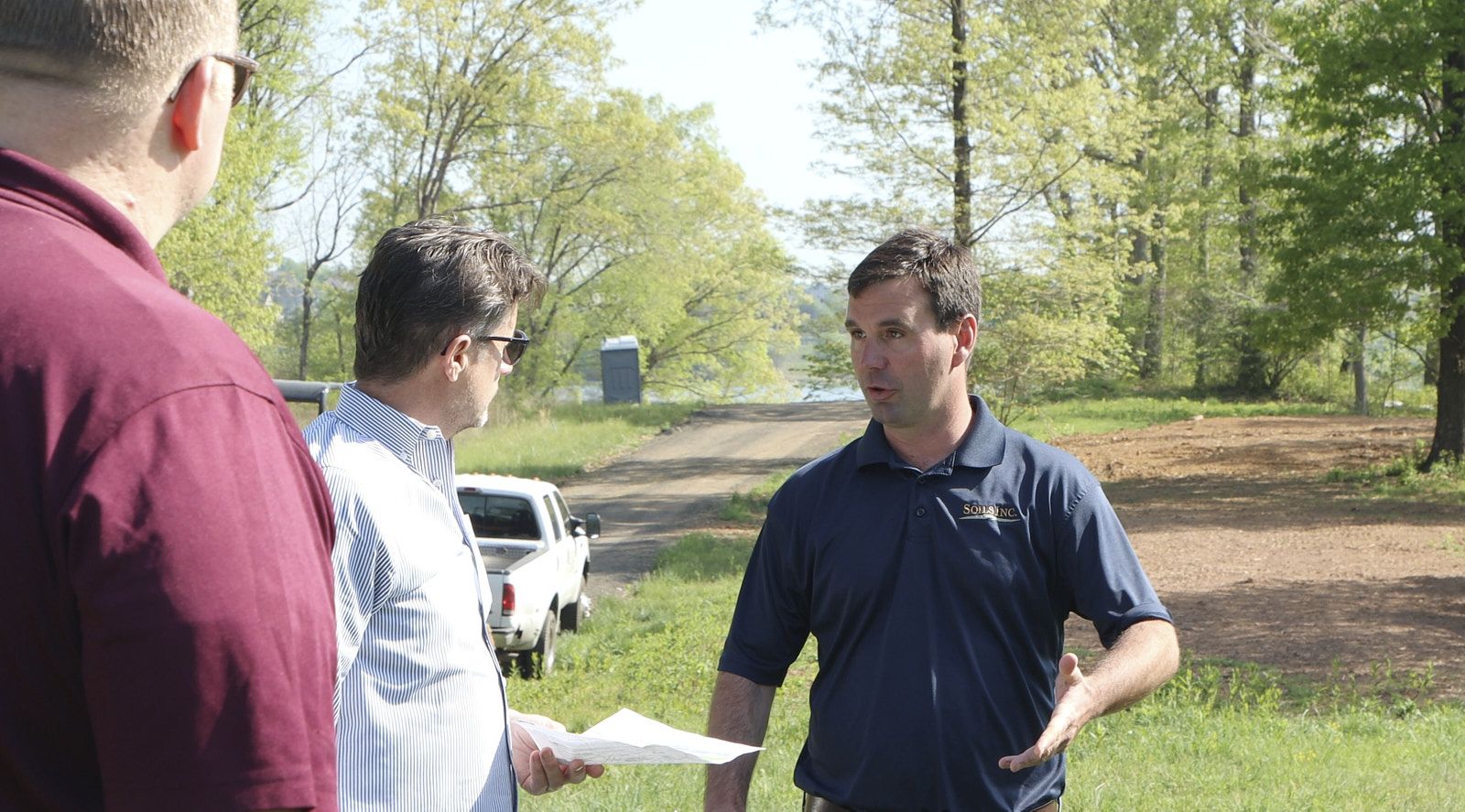 Three Senior Professionals From Soils Inc Standing At A Site Discussing While One Holds A Paper