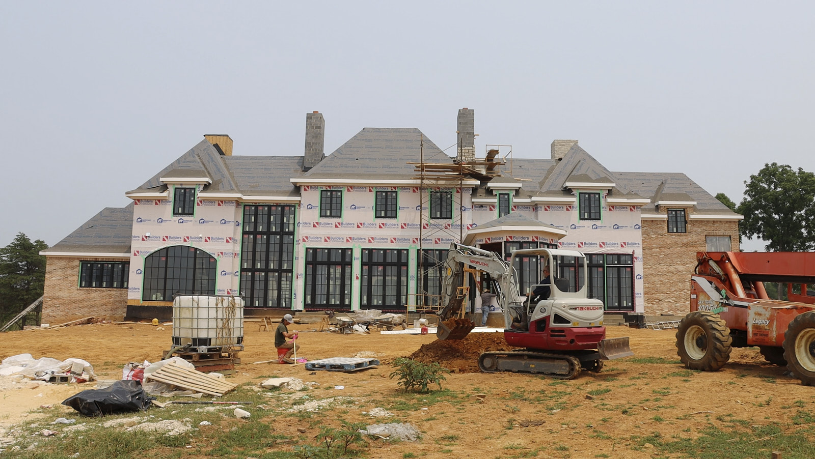 Wide Angle Shot Of A Newly Constructed Mansion With House Building Poles Remains And Few Tractors Working Outside By Soils Inc